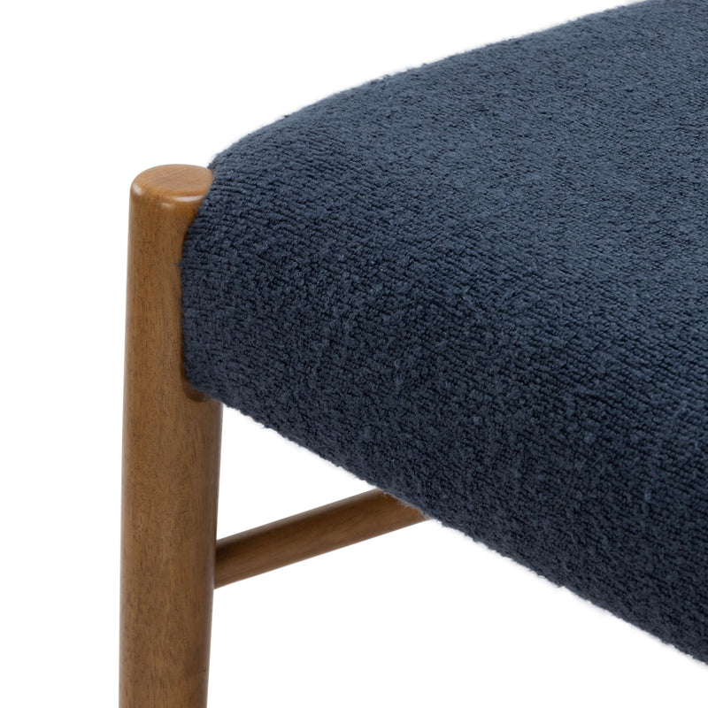 Close-up of navy blue textured upholstery on a round seat with walnut-toned wooden chair leg, modern stool detail