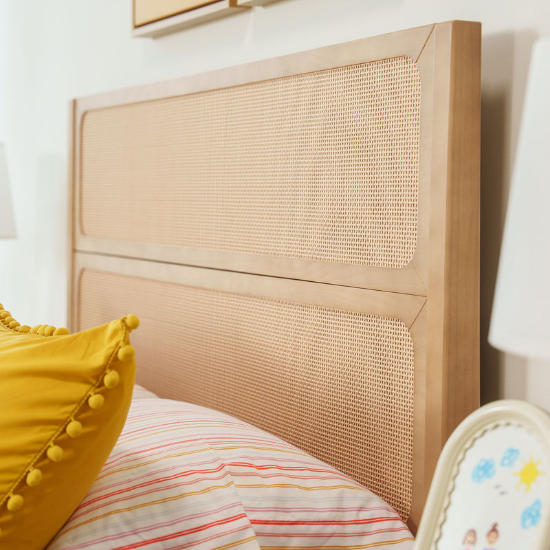 Close-up of natural wood rattan cane headboard with woven cane panel, yellow pom-pom pillow and striped bedding — boho bedroom decor