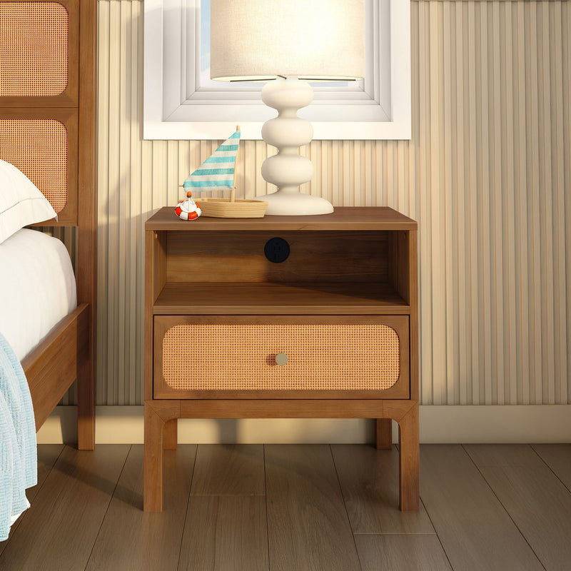 Coastal bedroom nightstand: wooden bedside table with rattan cane drawer, white ceramic lamp and small decorative sailboat with blue striped sail against beige shiplap wall and hardwood floor