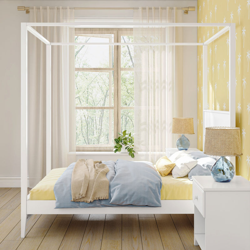 Bright modern children's bedroom with white canopy bed, pastel blue and yellow bedding, yellow palm-print wallpaper, sheer curtains over a wooden window, woven rattan bedside lamps and a potted plant on the windowsill