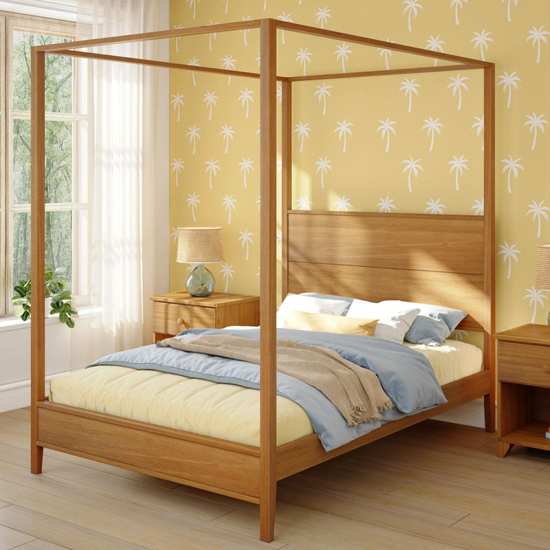 Wooden four-poster canopy bed in sunny bedroom with yellow palm-print wallpaper, natural wood nightstand, lamp and layered bedding