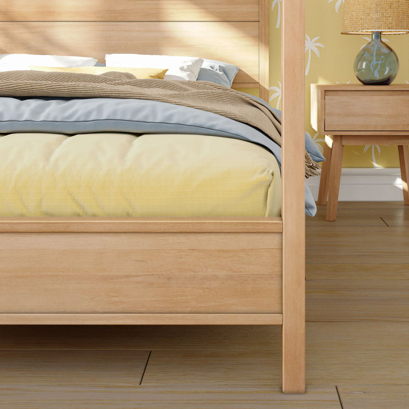 Cozy modern bedroom with light wood bed frame, yellow duvet, blue sheets, beige textured throw, white pillows and bedside table with glass lamp against palm-print wallpaper