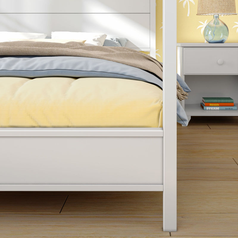 Cozy modern bedroom close-up: yellow comforter, blue blanket and beige knit throw on white bed frame, white nightstand with glass lamp and stacked books on hardwood floor