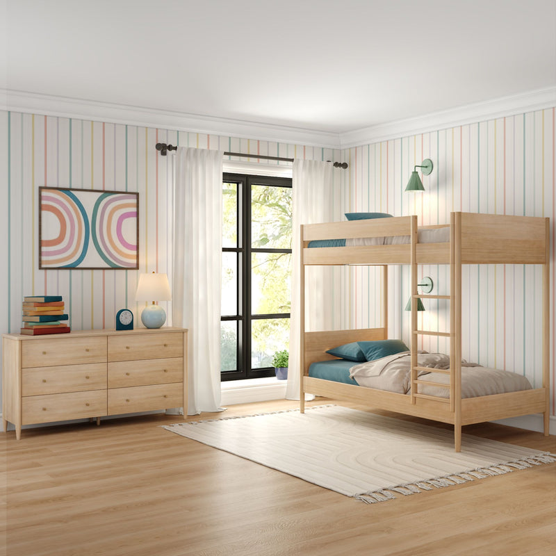 Bright kids' bedroom with light wood bunk beds, pastel striped wallpaper, dresser with lamp and books, and a large sunlit window