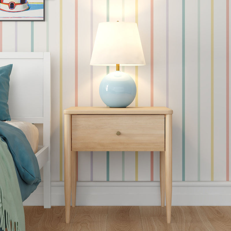 Light wood mid-century nightstand with blue ceramic table lamp in a minimalist bedroom featuring pastel vertical striped wallpaper, teal bedding and hardwood floor