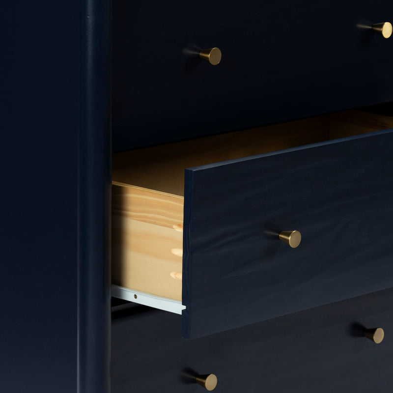Close-up of navy blue wooden dresser with open drawer revealing natural pine interior and brass round knobs, modern bedroom storage chest