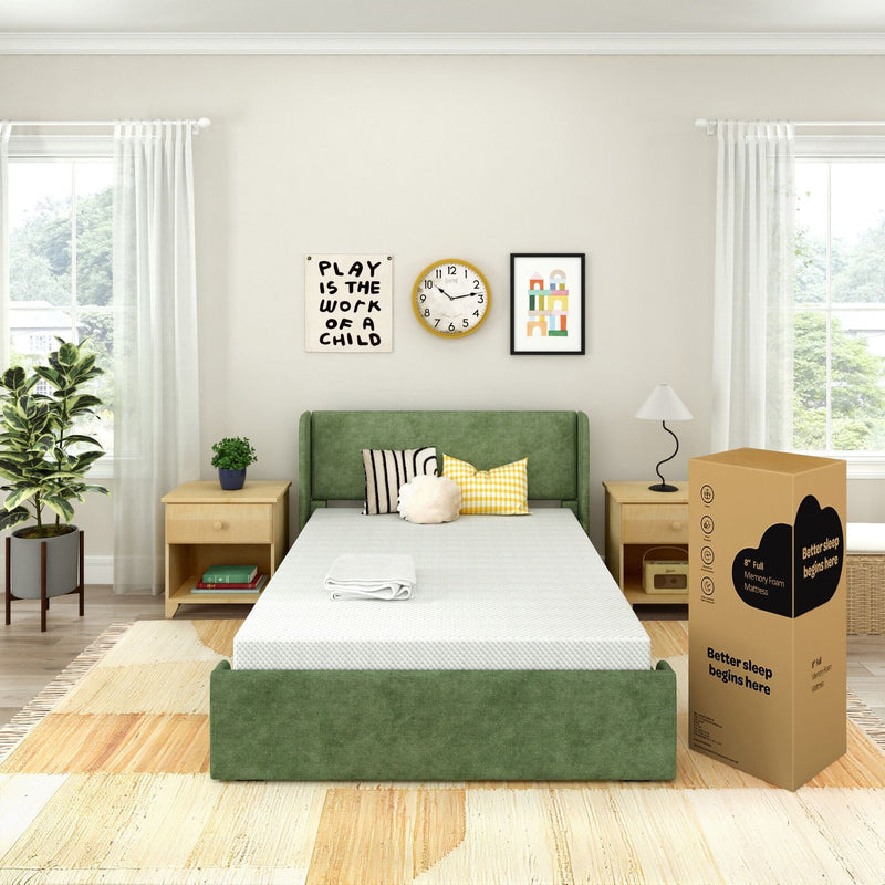 Full-size memory foam mattress-in-a-box beside a green upholstered bed in a bright modern bedroom with wooden nightstands, potted plant, decorative pillows and wall art reading "Play is the work of a child" — product photo for mattress, bedding and sleep accessories