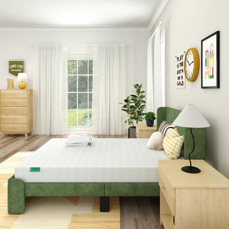 Minimalist bright bedroom with green upholstered platform bed and white mattress, wooden nightstand and dresser, large window with sheer curtains, indoor plants, decorative pillows and wall art.