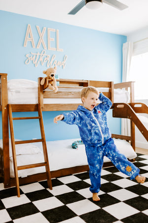 a little boy standing in front of a bunk bed in a blue sweatsuit