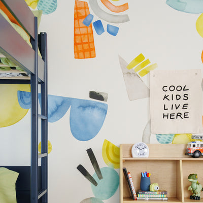 Children's bedroom decor: navy bunk bed, colorful abstract wall mural, wooden cubby shelf with clock, books, toy dinosaur and canvas sign reading 