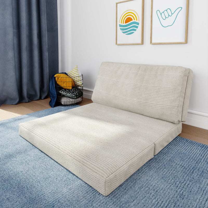 Minimal coastal-inspired living room corner with a beige low-profile floor mattress sofa on a blue rug, gray curtains, wire basket of decorative pillows and framed ocean wall art