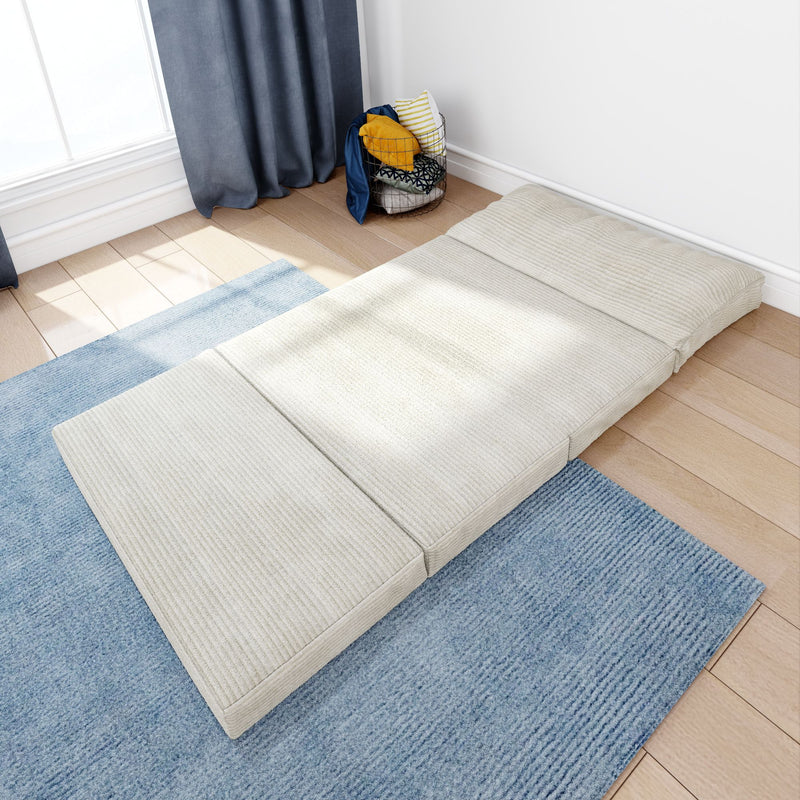 Cozy minimalist bedroom featuring a cream floor mattress on a textured blue rug beside a sunlit window, navy curtains, wooden plank floor and a wire basket of colorful throw pillows