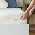 Person fitting a mattress protector on a bed for enhanced comfort and hygiene.