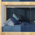 Lower bunk of wooden kids' bunk bed with navy textured headboard, blue gingham pillow, round navy cushion and blue blanket in a cozy children's bedroom