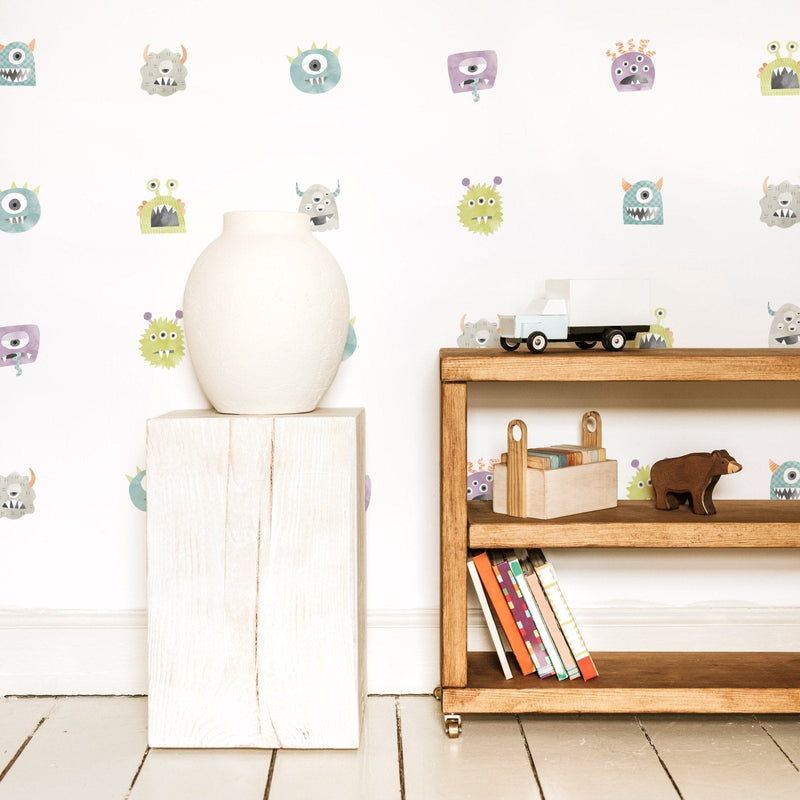 Minimalist kids room decor with pastel monster wall decals, white ceramic vase on wooden pedestal, wooden shelf with toy truck, children's books and wooden animal toys