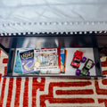 Open toddler bed drawer with children's books including Where the Wild Things Are, toy cars and a monster truck on red patterned rug