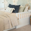 White wooden daybed with neutral beige quilt and decorative pillows against pastel world map wallpaper, nursery decor and neutral bedding