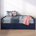 Children's navy storage daybed with blue bedding, pink throw and round white pillow, plush pink elephant toy on a light wood floor in a sunlit nursery