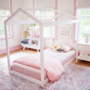 Pastel pink girls' bedroom with white house-frame twin bed, pink bedding, butterfly pillow, toy shelf and "Let's Be Mermaids" wall art
