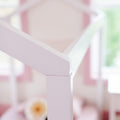 Close-up of white painted wooden crib railing in a pastel pink baby nursery, soft-focus interior with blurred floral accent and nursery decor