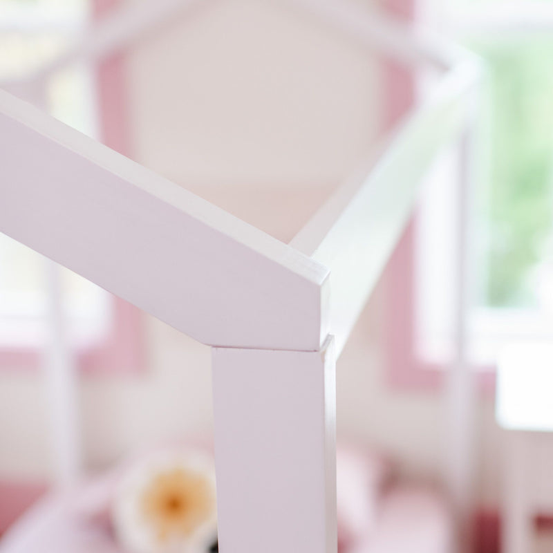 Close-up of white painted wooden crib railing in a pastel pink baby nursery, soft-focus interior with blurred floral accent and nursery decor