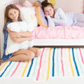Two smiling girls on a white bunk bed with pastel pillows and multicolored striped bedding — kids bedroom decor and sleepover idea