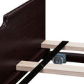 Close-up of espresso wood bed frame headboard with light pine slats, black center support strap and metal caster wheel