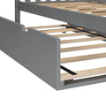 Gray wooden bed frame close-up showing exposed plywood slats and black central metal support strap on a modern platform bed base
