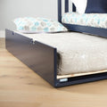 Navy blue pull-out trundle bed with twin mattress and patterned pillow on light hardwood floor, underbed storage for kids' bedroom
