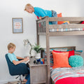 Gray wooden bunk bed with built-in desk in boys' bedroom — child reading at desk, another on top bunk, colorful pillows, toy car and Rubik's Cube, "Mini Man Cave" sign