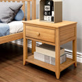 Light wood bedside table (oak nightstand) with single drawer and lower shelf holding storage boxes, styled next to a bed with blue-gray bedding