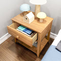 Modern oak nightstand with open drawer containing stacked books, small decorative birdhouse and mushroom-shaped lamps beside bed in a minimalist bedroom
