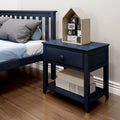 Navy blue nightstand with single drawer and lower shelf beside matching slatted bed on hardwood floor, topped with a beige house-shaped shelf holding black-and-white numbered blocks and gray pillows