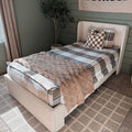 Cozy single bedroom with beige upholstered bed, brown and gray plaid bedding, checkered throw pillow, plush tan blanket, faux olive tree, green shiplap wall and neutral patterned carpet