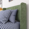 Close-up of green upholstered headboard with navy-and-white gingham bedding, blue accent pillows and a yellow bedside lamp in a modern bedroom