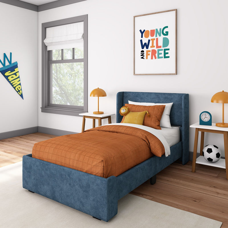 Modern kids bedroom with blue upholstered bed, orange quilted bedding, "Young Wild and Free" wall art, bedside lamp, nightstand and soccer ball