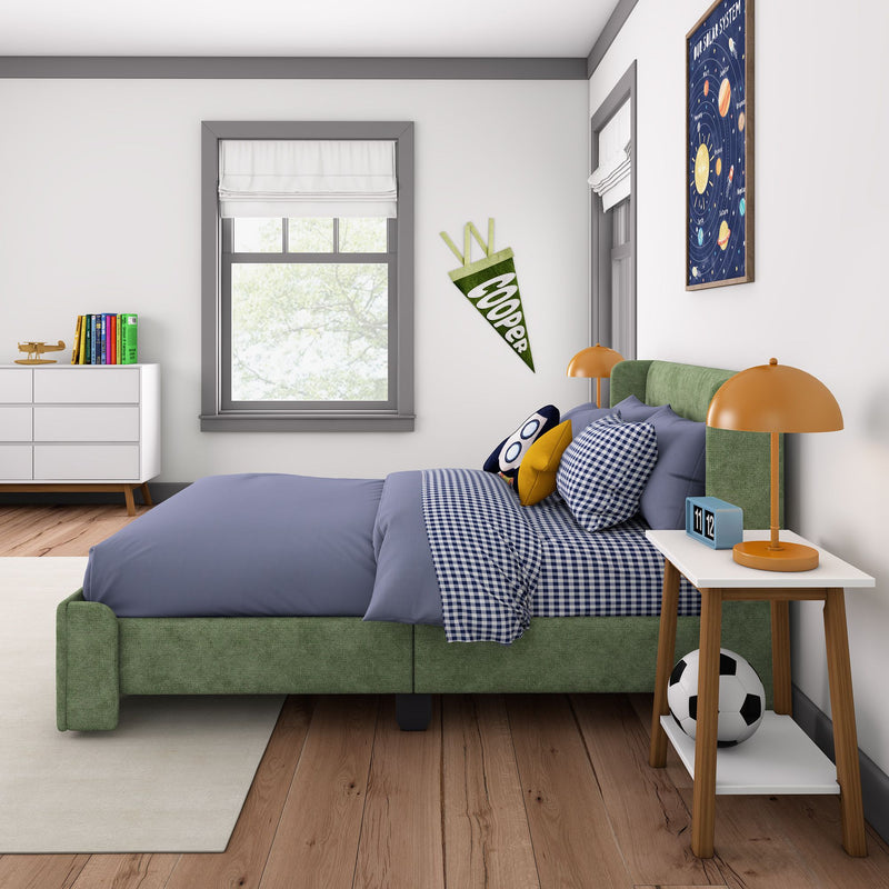 Modern kids bedroom interior with green upholstered bed and blue gingham bedding, orange bedside lamp, nightstand with flip clock, soccer ball, toy airplane on dresser, colorful books, white Roman shade window and framed solar system poster