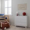 Bright boys' bedroom with white three-drawer dresser, wooden bunk bed, shuttered window, lamp and sports-themed decor including basketball plush and football bean bag.
