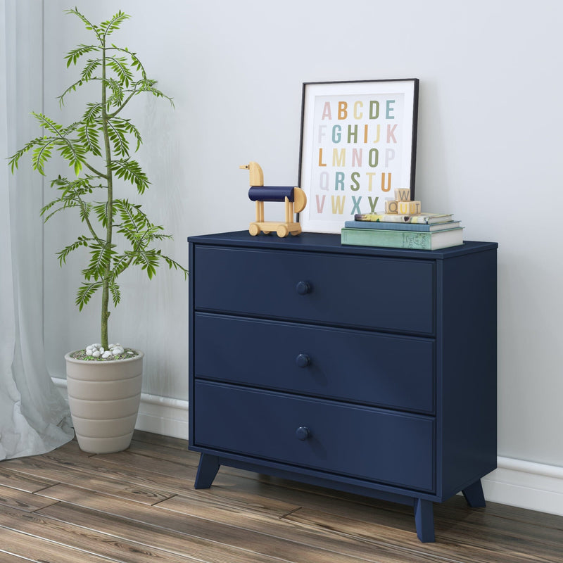 Navy blue three-drawer dresser in a modern nursery with wooden toy horse, framed colorful alphabet print, children's books and a potted plant on hardwood floor