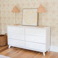 White six-drawer dresser on hardwood floor with rattan lamps, framed butterfly print, floral wallpaper and woven basket