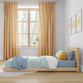 Children's bedroom with wooden bed, blue striped bedding, sun-shaped cushion, mustard curtains, nursery wall art and bright window