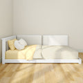 White daybed with yellow pillows and striped bedding against a beige wall on light hardwood floors, minimalist nursery decor