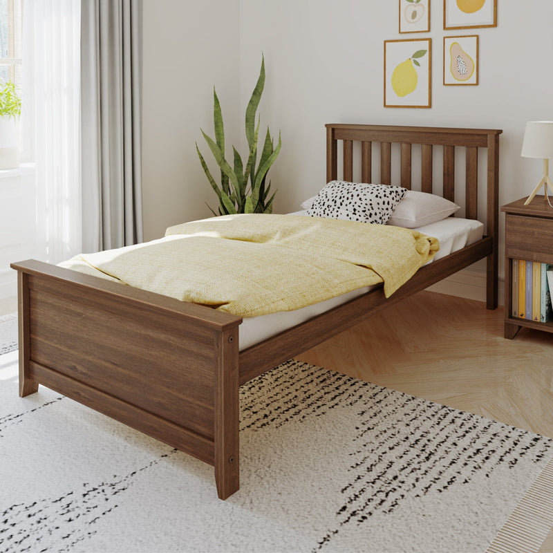 Cozy minimalist bedroom interior with wooden bed frame, yellow quilted bedding, spotted accent pillow, snake plant, framed fruit wall art, nightstand with lamp and books, and soft natural light