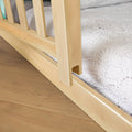 Close-up of light oak wooden bed frame with vertical slats and white quilted mattress cover on hardwood floor
