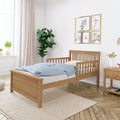 Bright modern nursery with natural wood toddler bed, blue polka-dot duvet, framed animal print gallery wall, potted fiddle-leaf fig and sunlit window
