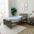 Bright modern nursery with gray wooden toddler bed, blue polka-dot duvet, gold-framed animal prints, potted plants and soft natural light