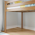 Close-up of a natural wood loft bed frame with slatted guardrail, yellow pillow and blue knit blanket in a minimalist modern bedroom with light hardwood floors and gray curtains