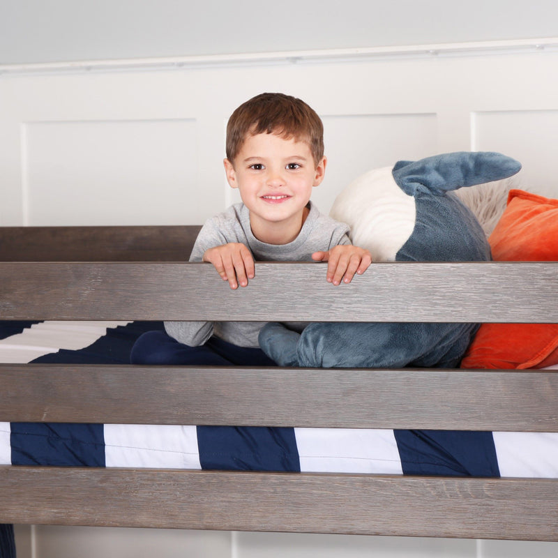 Smiling young boy leaning on a wooden bunk bed with navy-striped bedding and a plush shark pillow in a cozy kids' bedroom