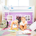 Two young girls drawing under a white loft bed with a purple playhouse curtain, colorful rug, slide and backpack in a bright kids’ bedroom