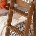 Close-up of wooden high chair steps and ladder detail in a cozy nursery setting with a checkered blanket and plush pumpkin toy